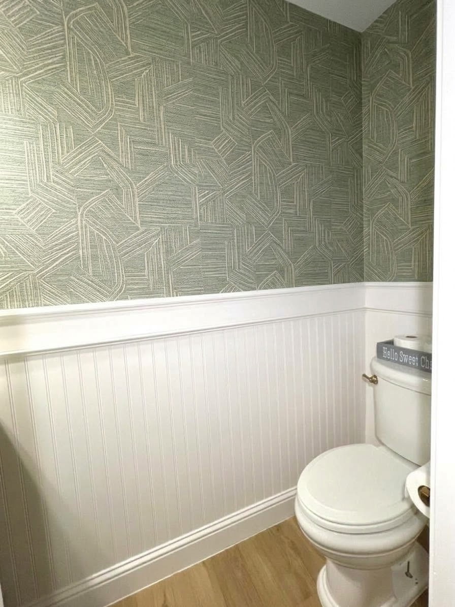 Green geometric wallpaper above white bathroom paneling