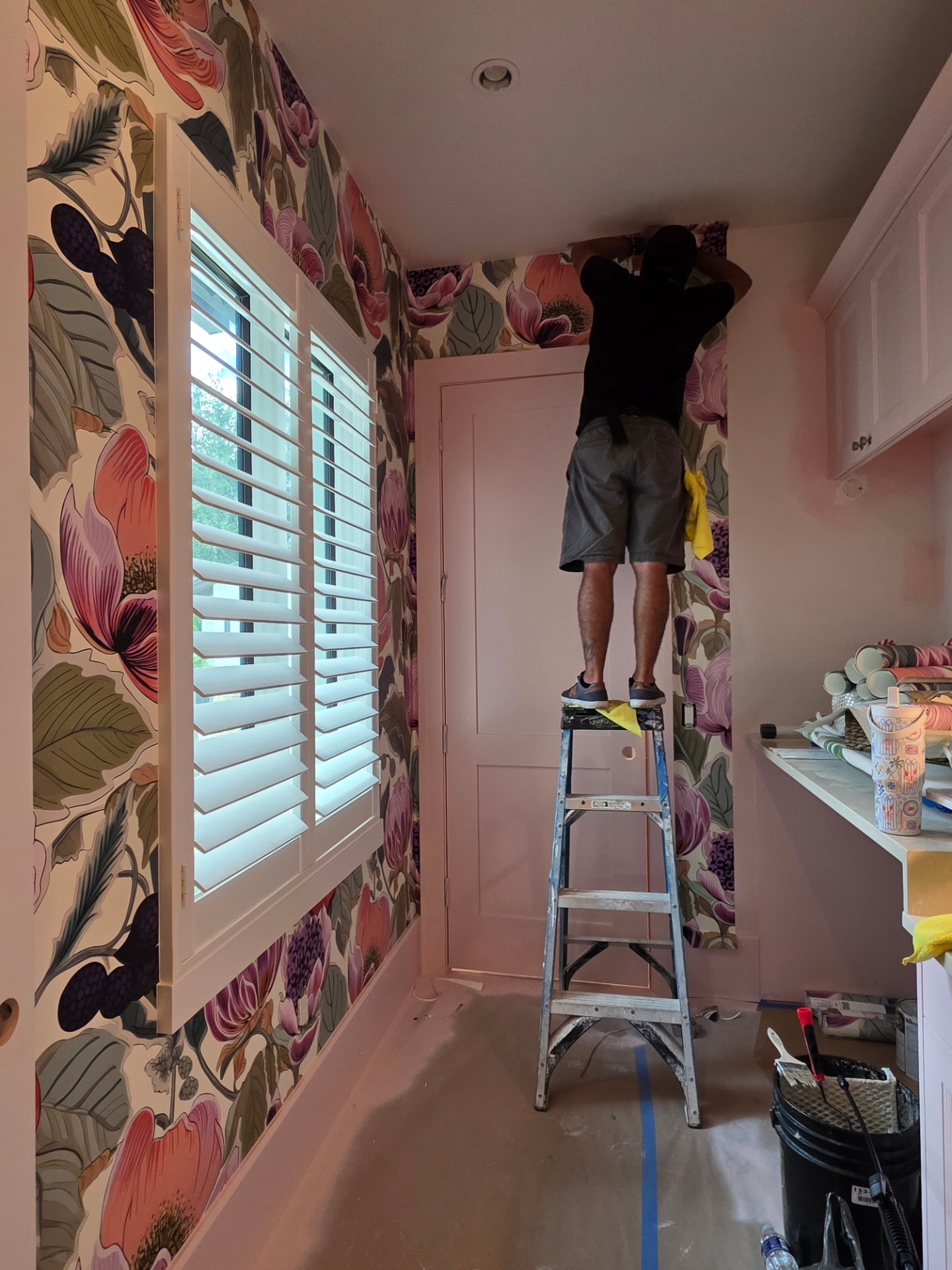 Installer fitting floral wallpaper above a doorway beside a window