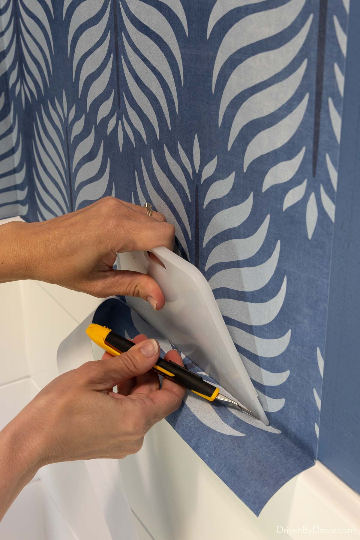 Close-up of hands trimming blue patterned wallpaper