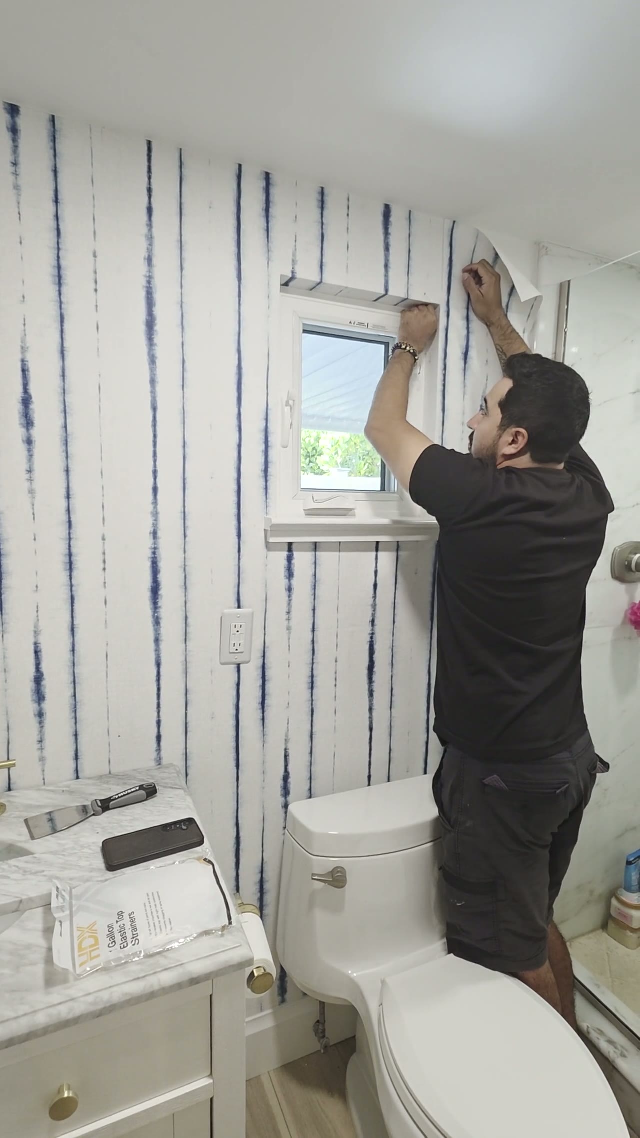 Video of an installer fitting blue and white striped wallpaper around a bathroom window